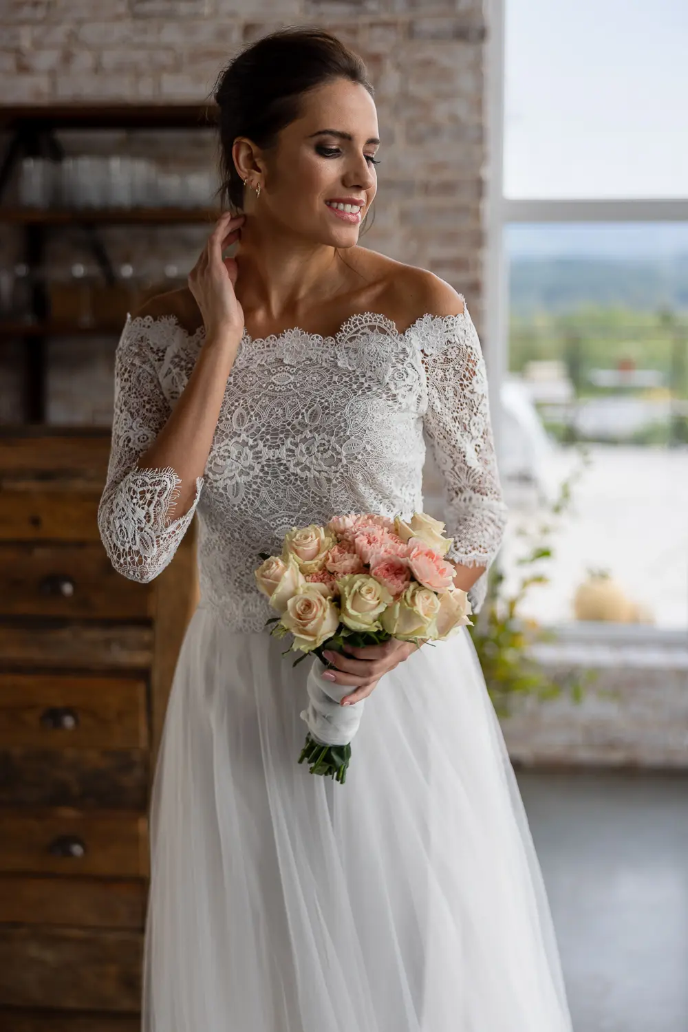 Braut im Off-Shoulder-Spitzenkleid mit langen Ärmeln und Brautstrauß