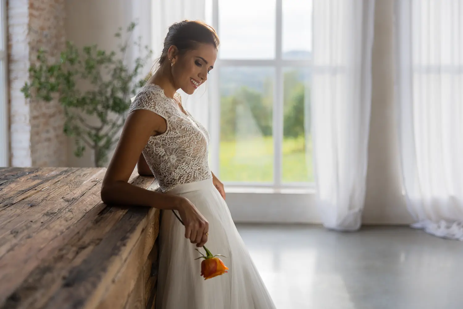 Braut im Spitzenkleid sitzt am Fenster